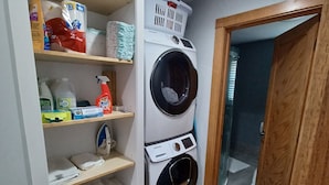 Ein Waschraum mit einer Samsung Waschmaschine und einem Trockner mit Frontöffnung, Regalen für Reinigungsmittel und einem Holzboden.