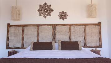 A bedroom with a large bed, two decorative wall hangings, and a hanging light fixture.