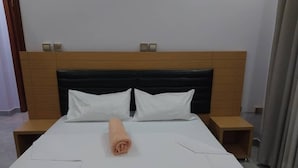 Un lit bien fait, avec du linge de lit blanc et une serviette enroulée, deux tables de chevet et une tête de lit en bois.