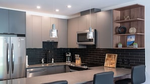 A modern kitchen with stainless steel appliances, a black backsplash, and a wooden island with bar seating. - Alpine Haven by Revelstoke Vacations (Revelstoke)