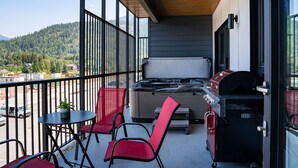A balcony with a hot tub, grill, and seating area with a view of the mountains. - Alpine Haven by Revelstoke Vacations (Revelstoke)