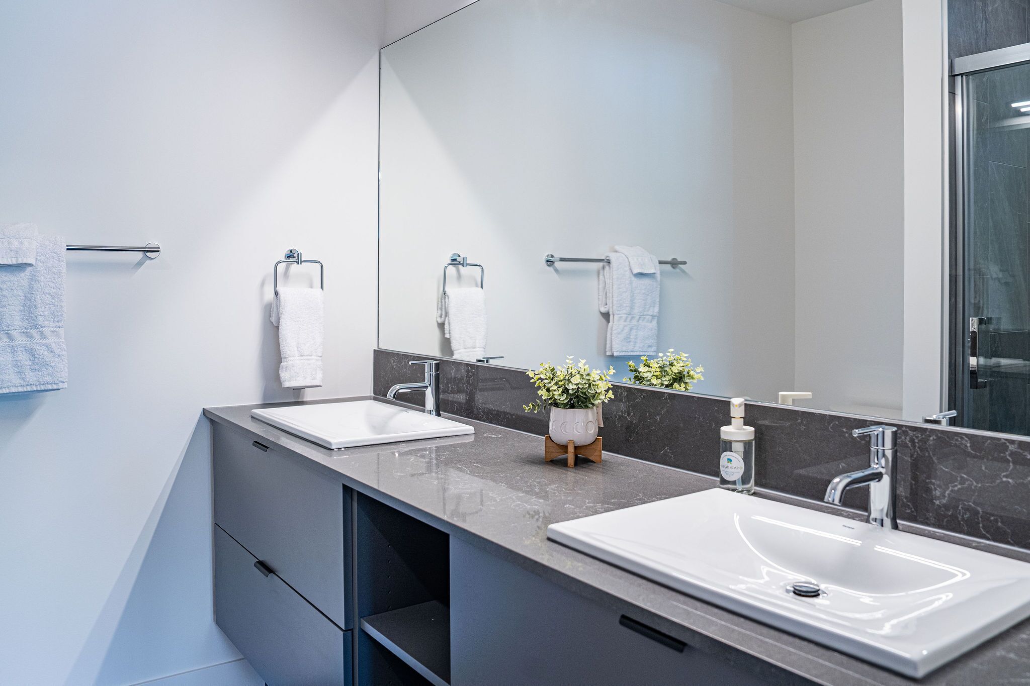 Une salle de bain moderne avec deux lavabos, un grand miroir et une douche.