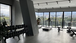 A modern gym with a treadmill, dumbbells, and a large window offering a city view. - Modern studio with parking - Murphy bed (Quito)