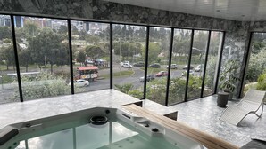 A modern bathroom with a large bathtub, marble walls, and a view of a busy street through large windows. - Modern studio with parking - Murphy bed (Quito)