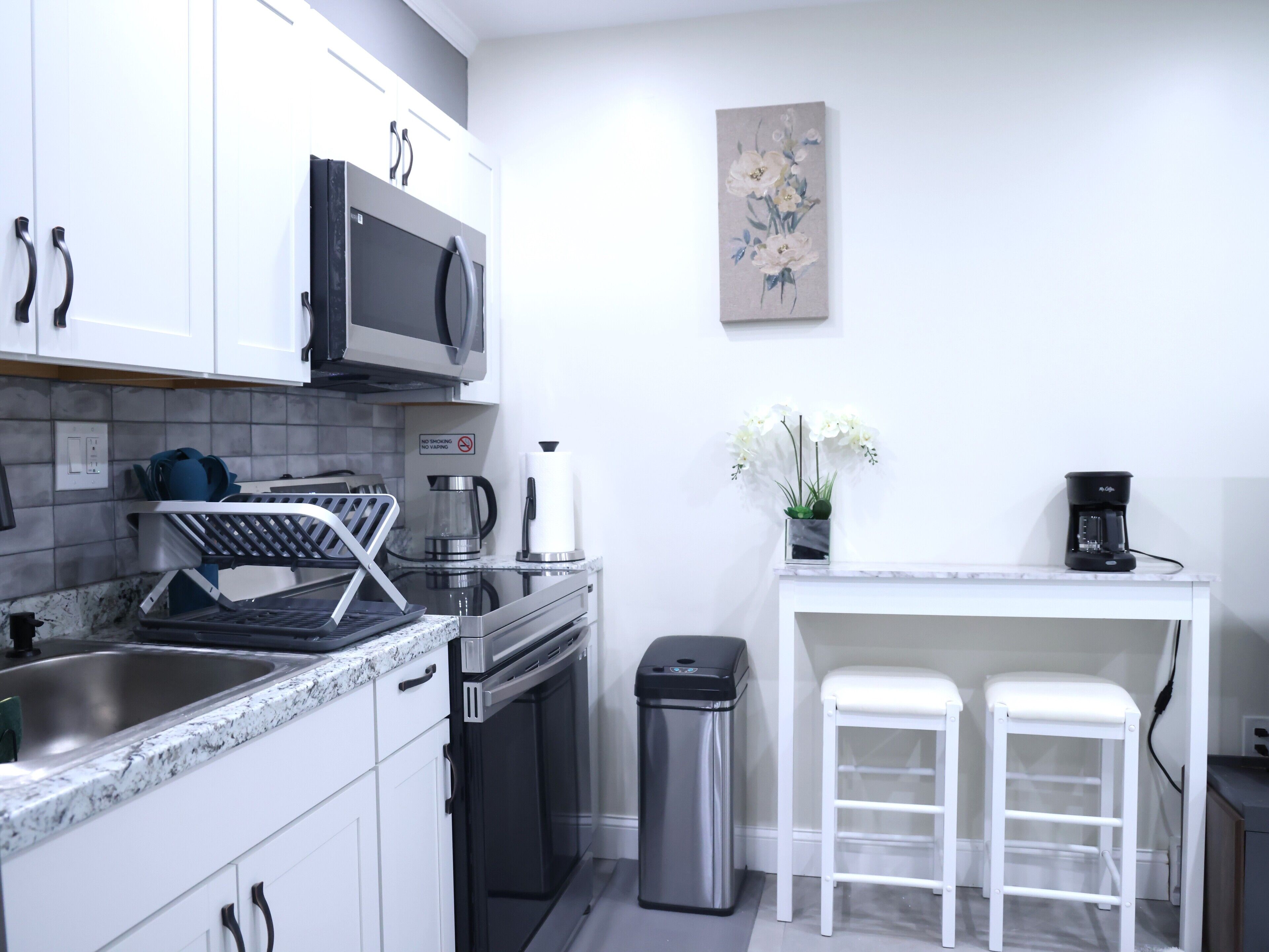 A modern kitchen with white cabinets, a stainless steel sink, a microwave, a coffee maker, and a trash bin.