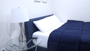 A hotel room with a bed, a bedside table with a lamp, and two wall-mounted flower paintings. - My Cozy-Snug Place - 1Brd - 8 mins to EWR (Elizabethport, NJ)