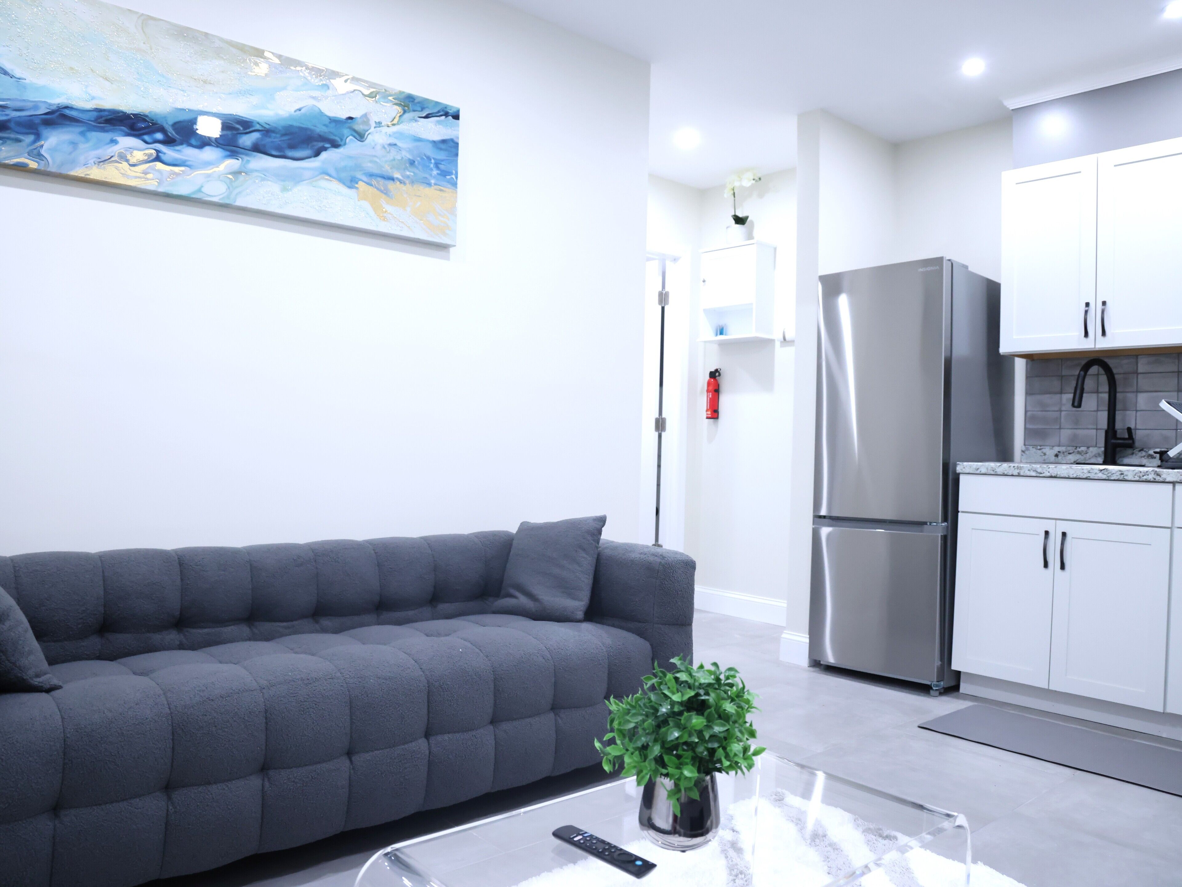 Una sala de estar moderna con un sofá gris, una mesa de centro con un control remoto y una planta en maceta.