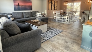 Ein modernes Wohnzimmer mit Ecksofa, Essbereich mit Tisch und Stühlen sowie Küchenzeile mit Arbeitsfläche und Spüle.