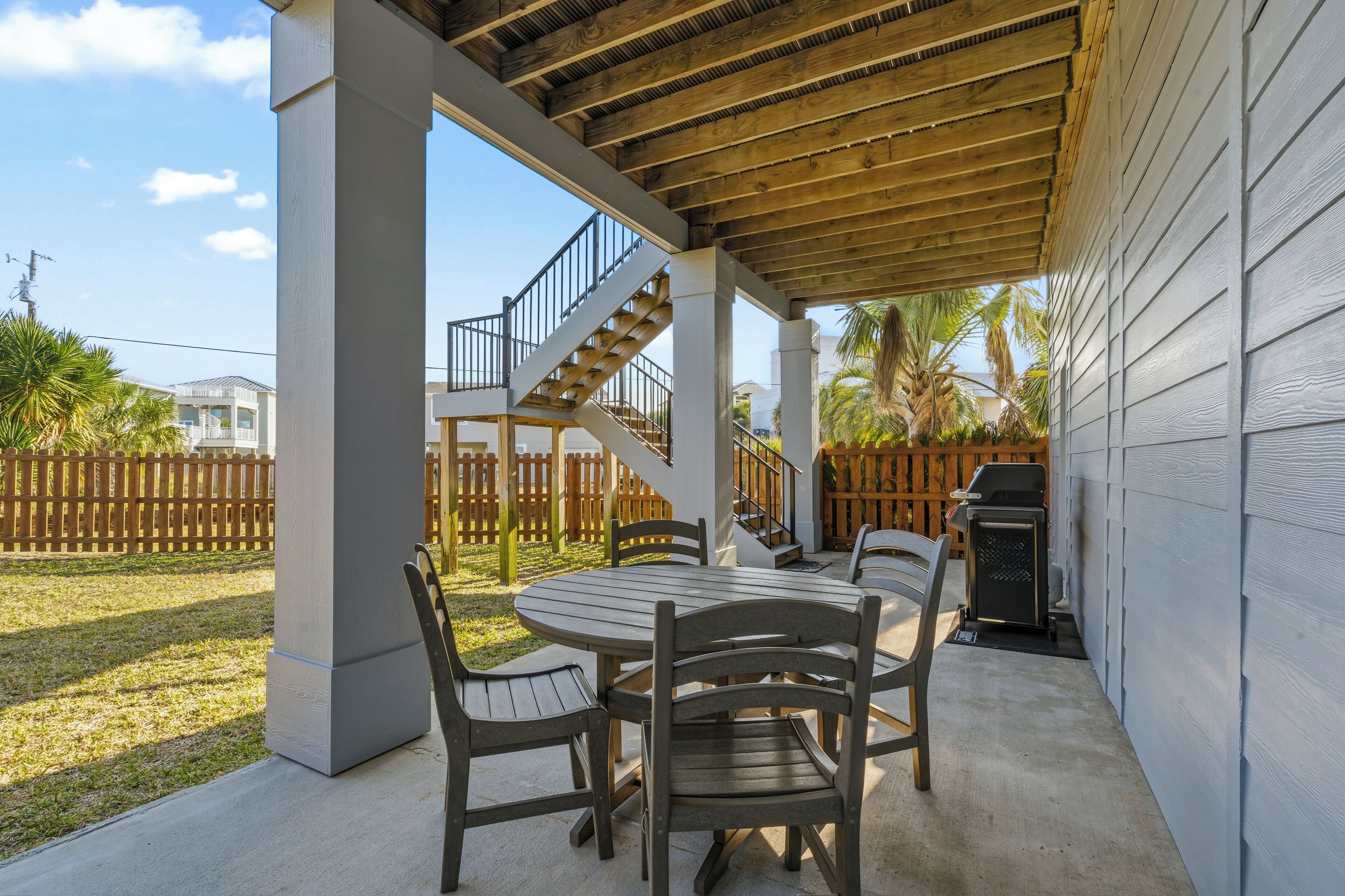 Une terrasse extérieure avec une table ronde et des chaises, un escalier en bois et un barbecue.