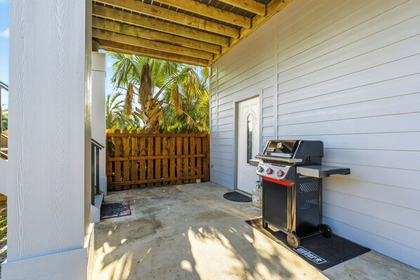 Een overdekt terras met een grillplaats en een houten omheining.