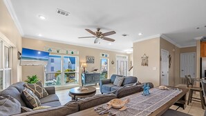 A spacious living room with a large sofa, a dining table, and a ceiling fan.