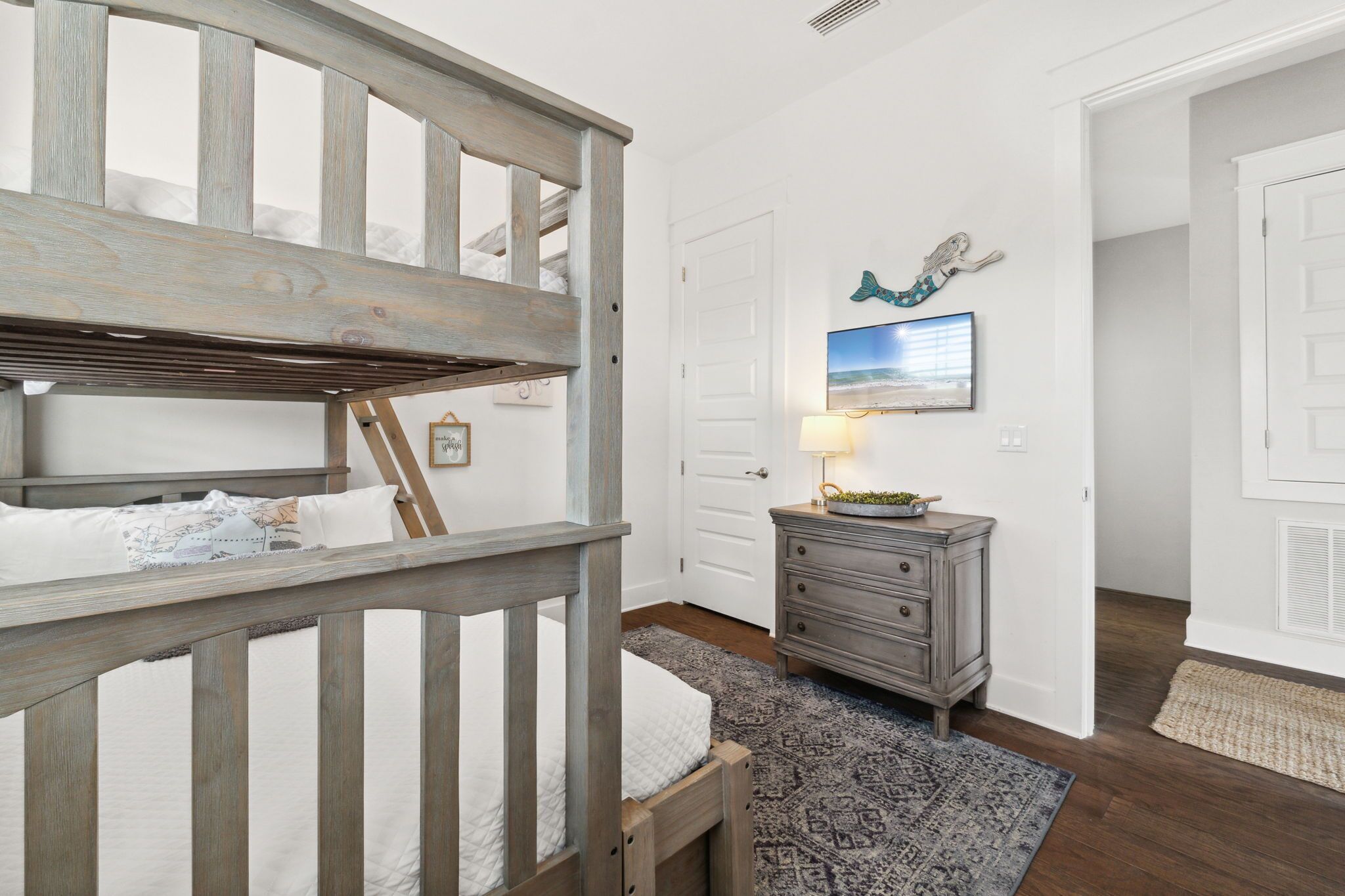 A bedroom with a bunk bed, a dresser, a rug, and a wall-mounted TV.