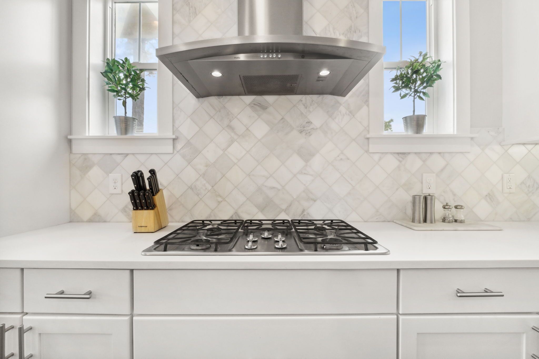 A kitchen with a gas stove, white cabinets, and a stainless steel range hood.
