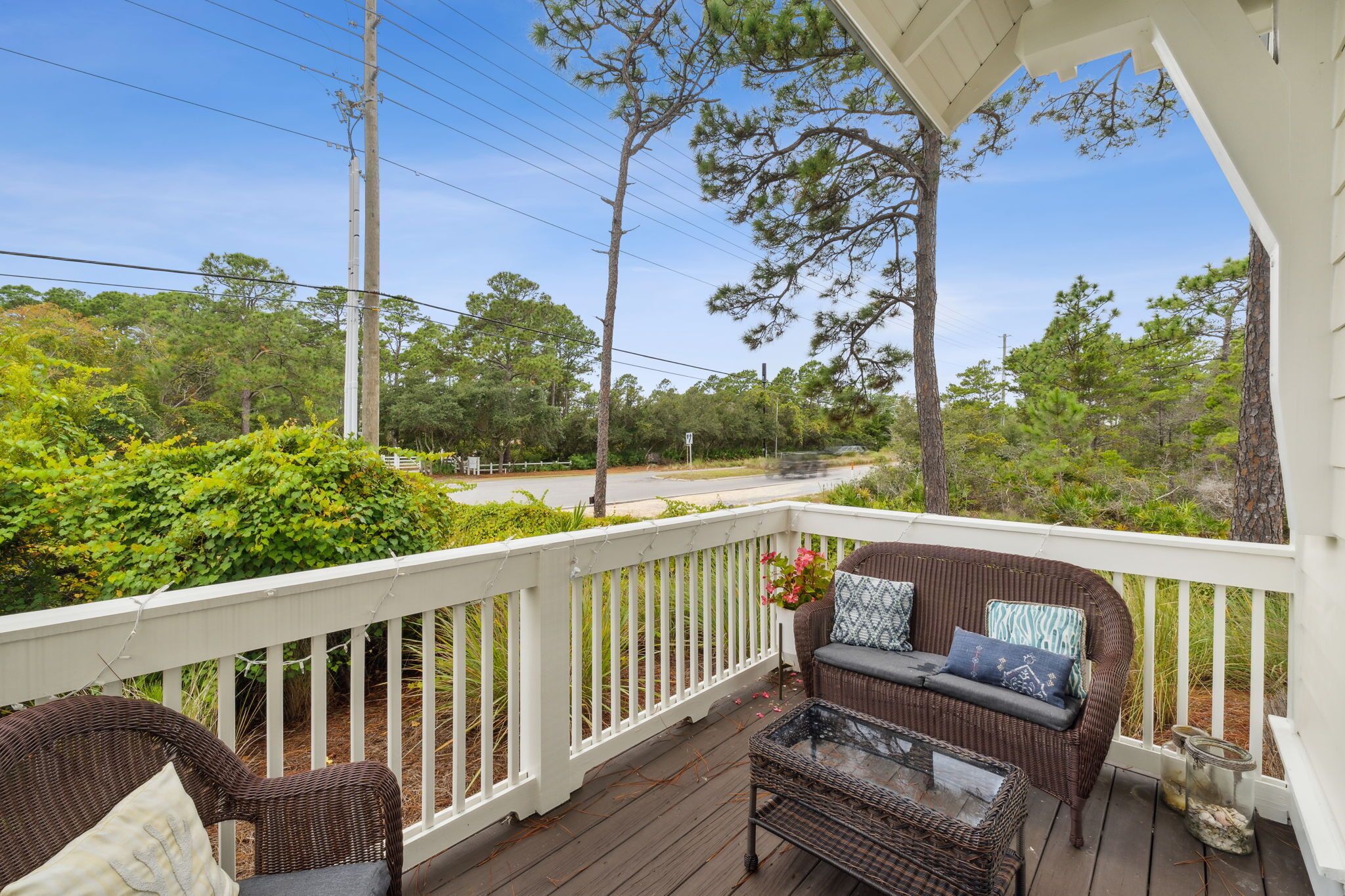 A covered porch with wicker furniture and a view of a road and trees.
