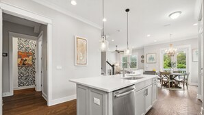 A modern kitchen with a central island, pendant lights, and a view to the dining area.