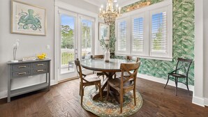 A dining area with a round table, chairs, a chandelier, and a wall with a tropical leaf pattern.