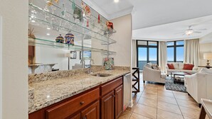 Cozinha moderna com bancadas de granito, uma vitrine de vidro e uma sala de jantar com sofá branco e mesa de centro.