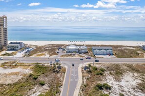 A coastal hotel with a parking lot, a road leading to the beach, and a view of the ocean.