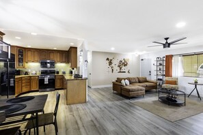 Eine moderne Küche mit integrierten Geräten, ein Essbereich mit Tisch und Stühlen, ein Wohnzimmer mit Sofa und Couchtisch sowie ein Deckenventilator.