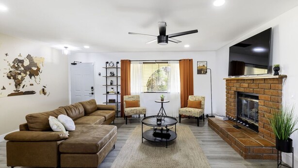 Una sala de estar con un sofá seccional marrón, una mesa redonda de centro, una chimenea y un ventilador de techo.