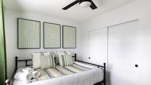 Una cama bien hecha con un edredón a rayas, un ventilador de techo y tres cuadros decorativos con diseños.
