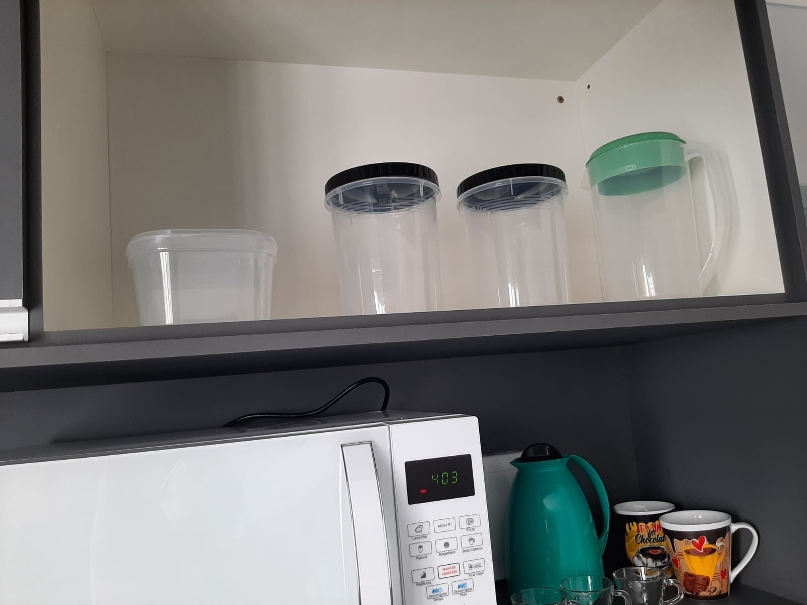 Una kitchenette con microondas, una tetera verde y cafetera. Hay tres recipientes transparentes en la alacena superior.