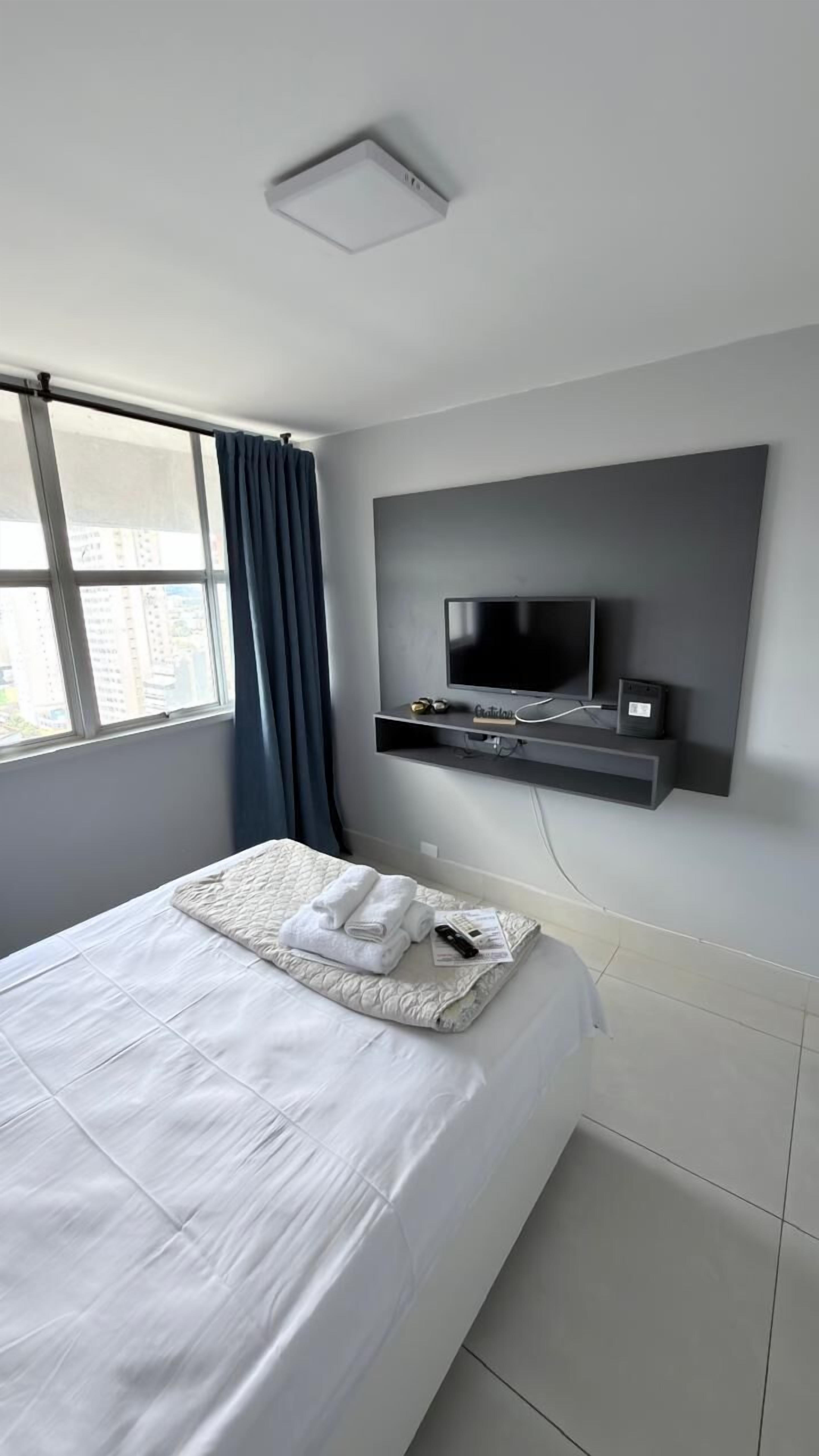 A modern hotel room with a large bed, a mounted TV, and a window with curtains.