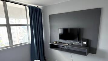 A modern hotel room with a large bed, a mounted TV, and a window with curtains.