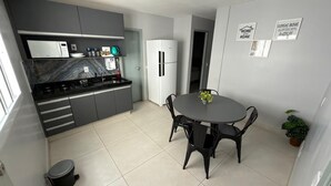 A modern kitchen with grey cabinets, a black countertop, and a white refrigerator. There is a dining table with chairs and a small potted plant. - Luxo e conforto  (Goiania)