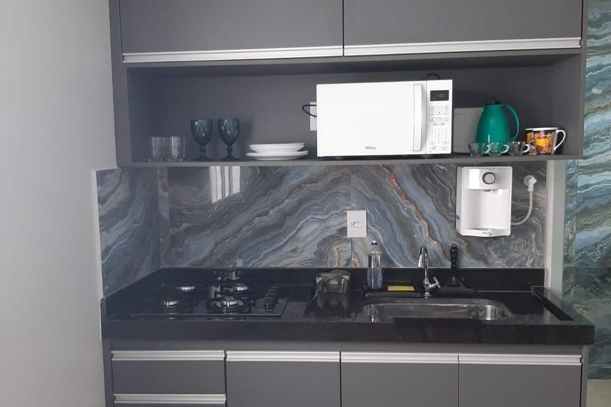 A modern kitchen with grey cabinets, a marble backsplash, a built-in microwave, and a coffee machine.