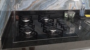 A kitchen with a black stove top, marble backsplash, and a white shelf with decorative glassware. - Luxo e conforto  (Goiania)