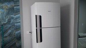 A white refrigerator in a room with a marble-patterned door and a bed in the background. - Luxo e conforto  (Goiania)