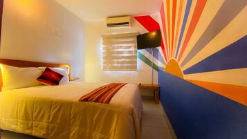 Una habitación de hotel con una cama, una mesita de noche, un equipo de aire acondicionado, un televisor montado en la pared y una ventana con persianas.