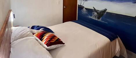Habitación de hotel con cama, almohadas y un mural en la pared que muestra un océano a la luz de la luna.