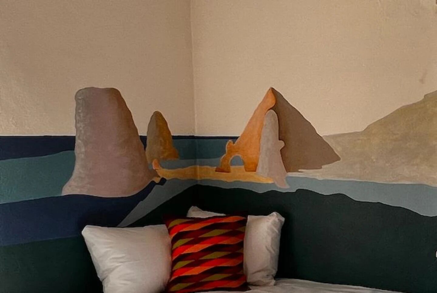 A room with a bed, pillows, and a wall mural depicting a mountainous landscape.