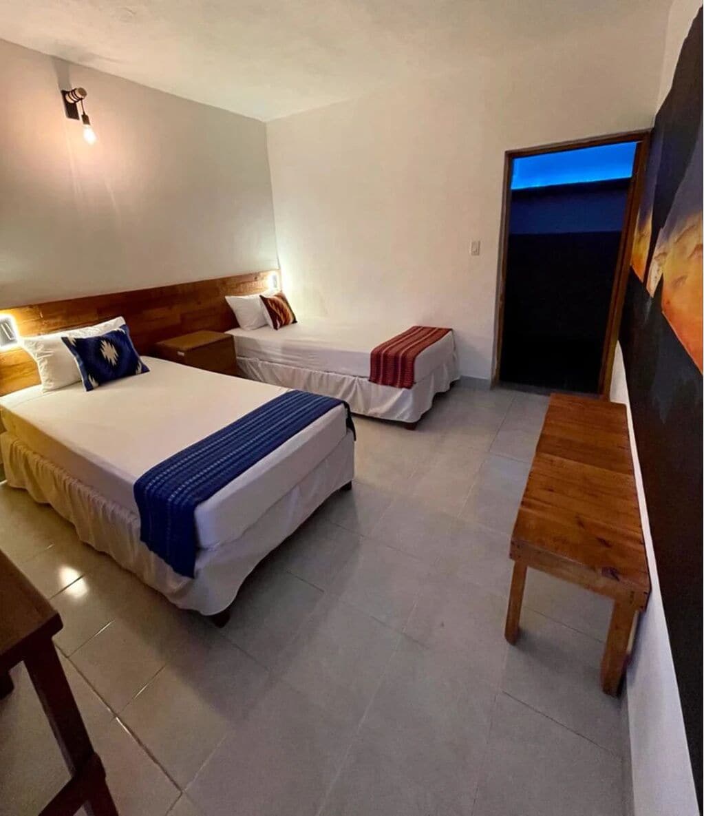A hotel room with two beds, a wooden bench, and a door leading to a balcony.