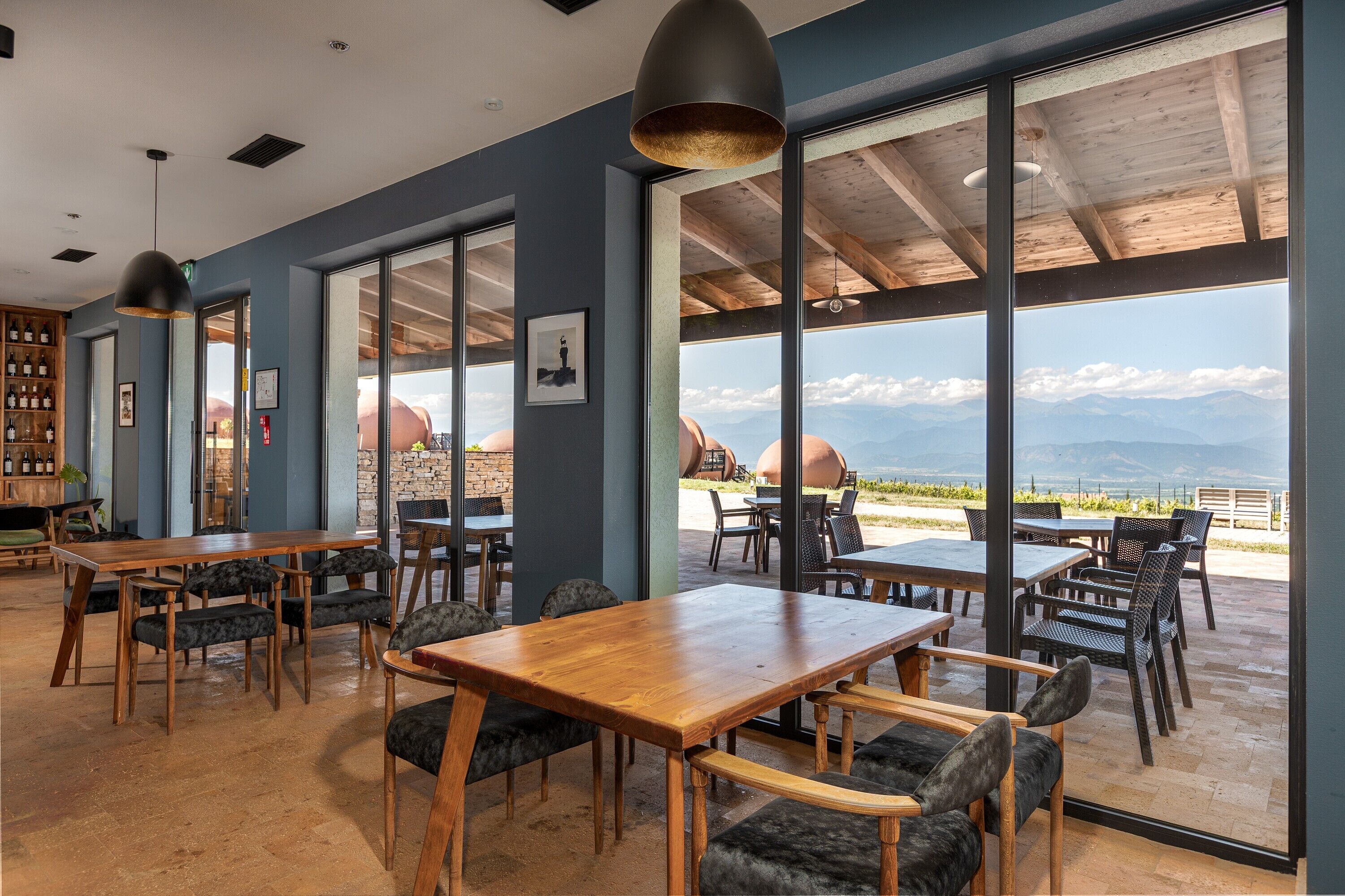 Um restaurante com grandes janelas, mesas e cadeiras de madeira.