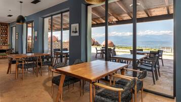 Um restaurante com grandes janelas, mesas e cadeiras de madeira.