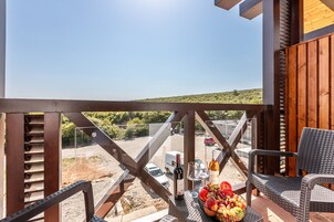 A balcony with wicker furniture, a table with a bottle of wine, glasses, and a fruit basket.