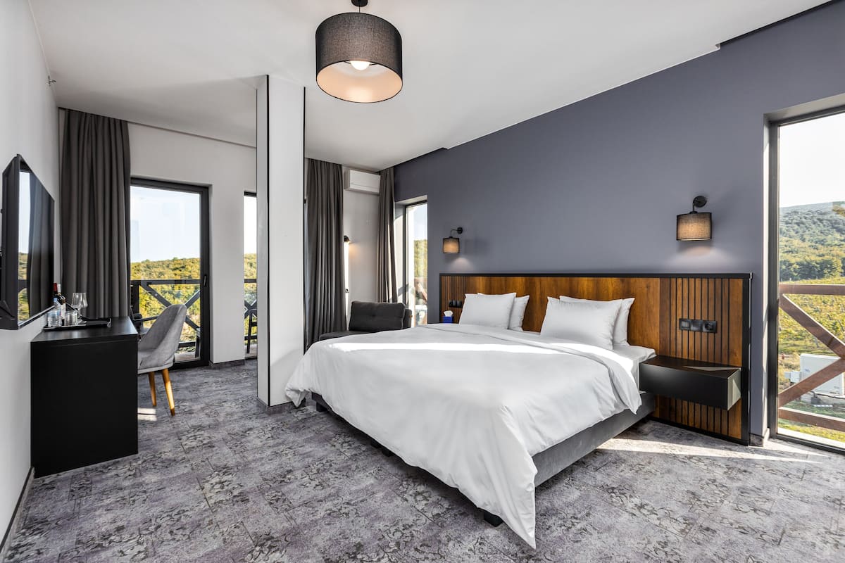 A modern hotel room with a large bed, a desk, and a view of the outdoors.