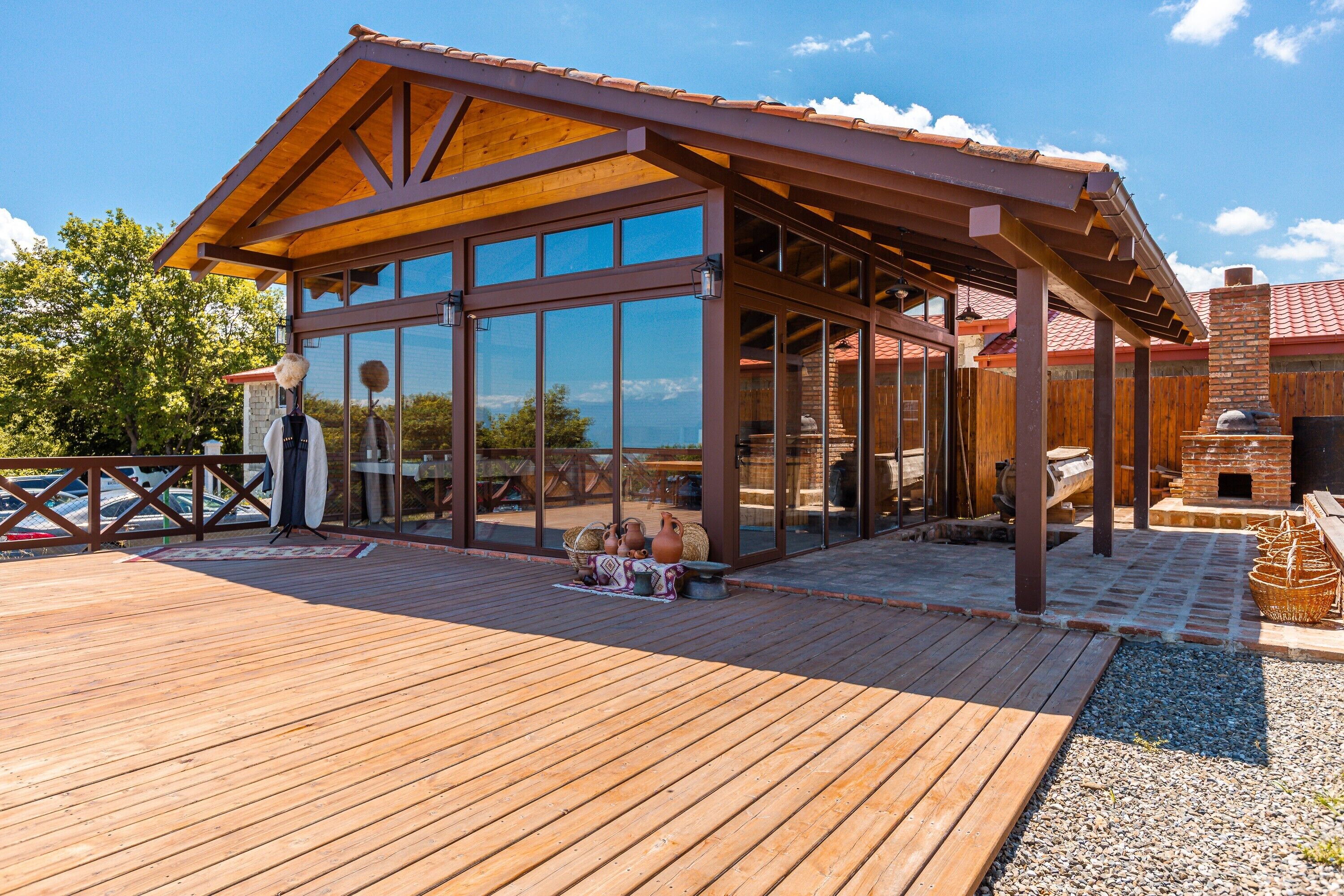 Une terrasse en bois avec un bâtiment à ossature de verre, une cheminée en briques et des sièges d’extérieur.