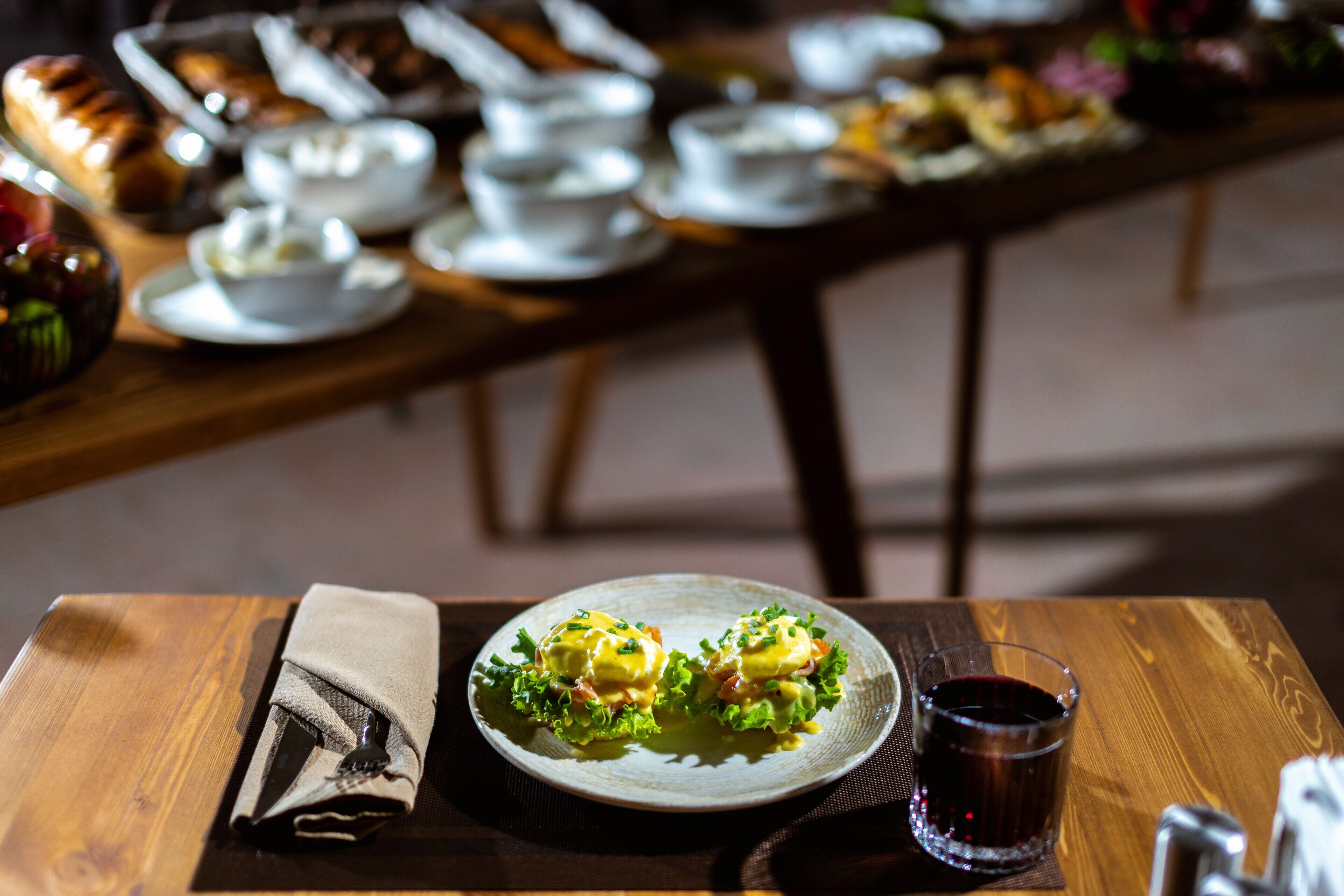 A wooden table with a plate of food, a napkin, and a glass of red drink.
