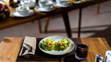 A wooden table with a plate of food, a napkin, and a glass of red drink.