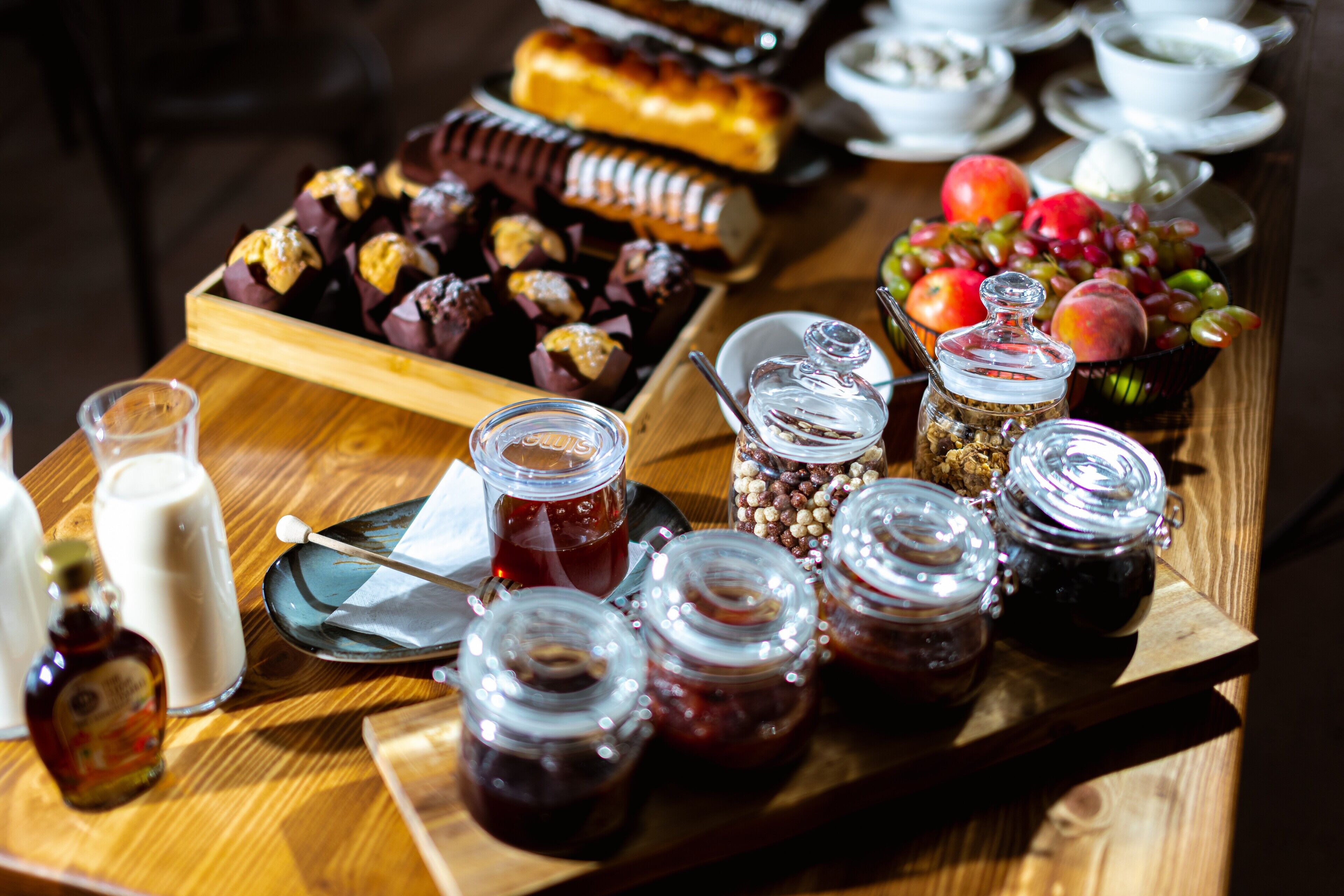 A wooden table with various food items, including pastries, fruits, and jars of preserves.