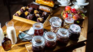 A wooden table with various food items, including pastries, fruits, and jars of preserves.