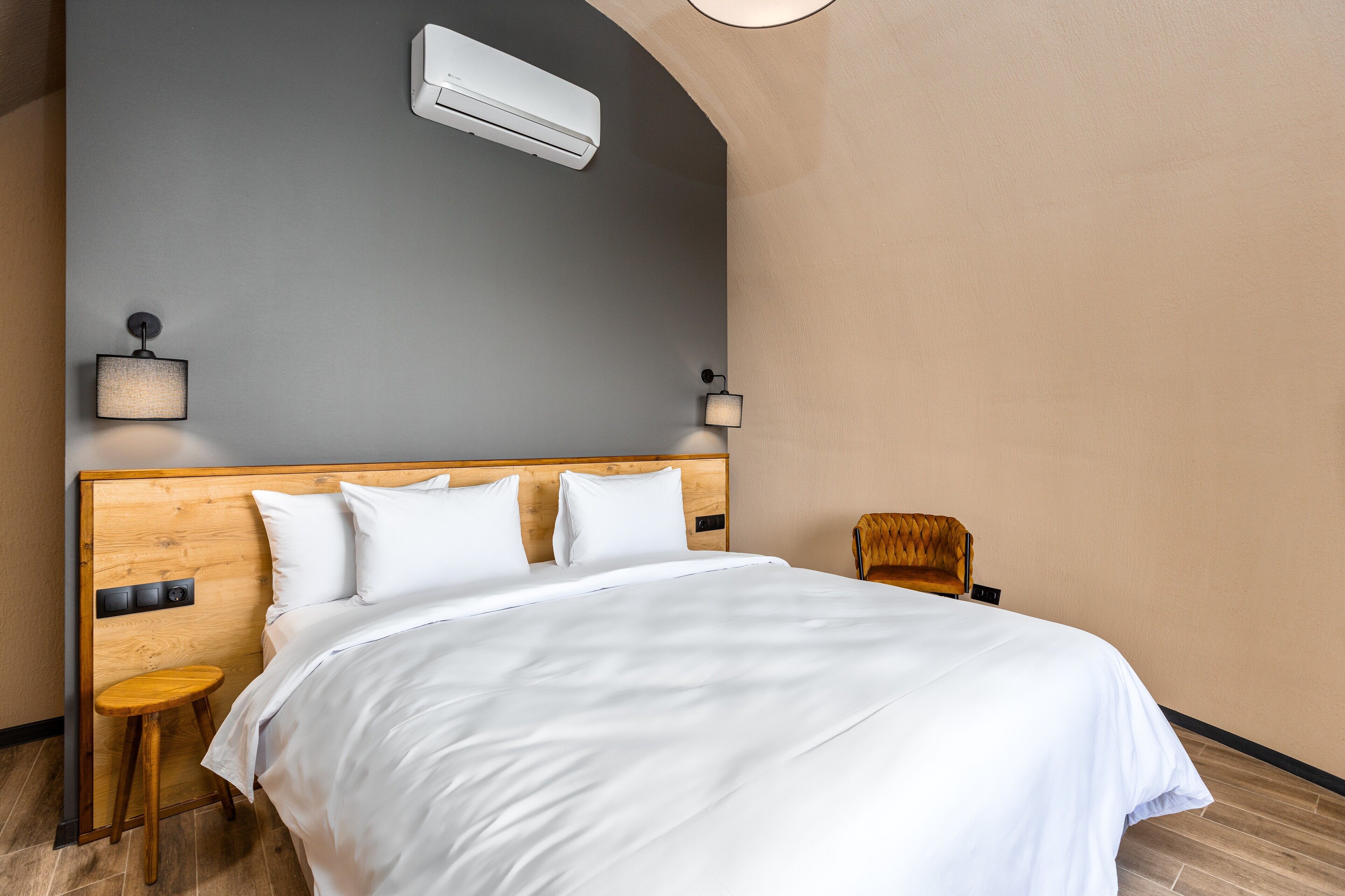 A neatly made bed with white linens, a wooden headboard, and two wall-mounted lamps.