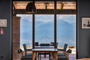 Un comedor con mesa y sillas, una lámpara colgante y vistas a las montañas a través de amplios ventanales.