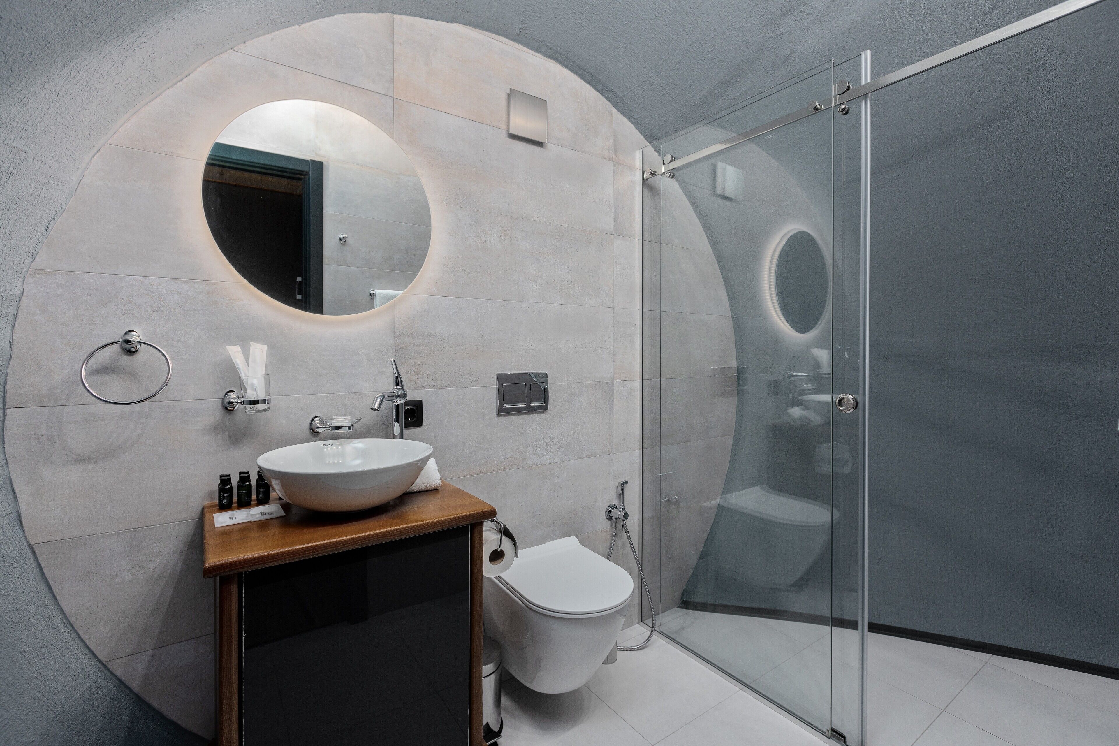 A modern bathroom with a round mirror, a white sink, and a glass-enclosed shower.