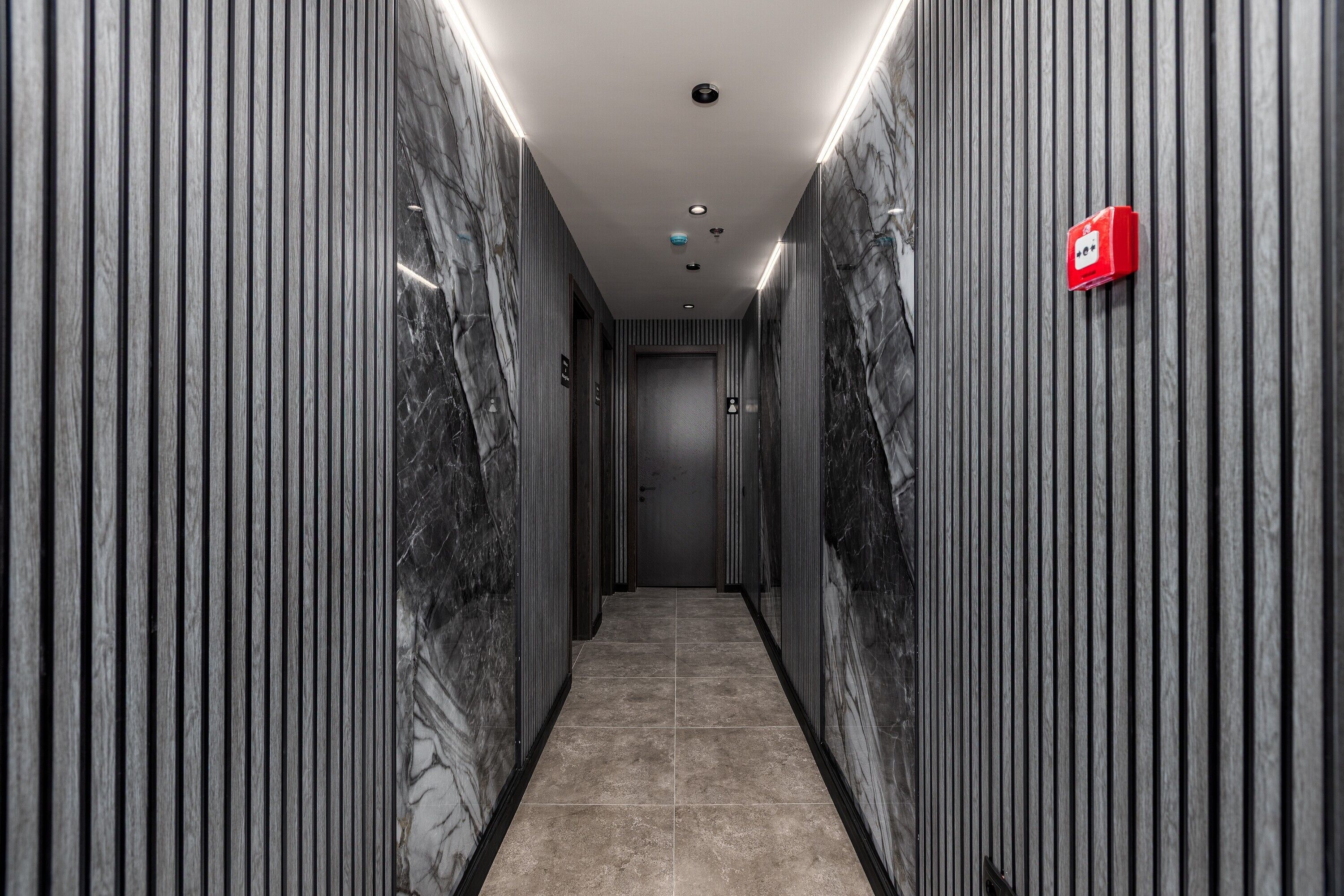 A modern hallway with marble walls and a tiled floor, leading to a door at the end.