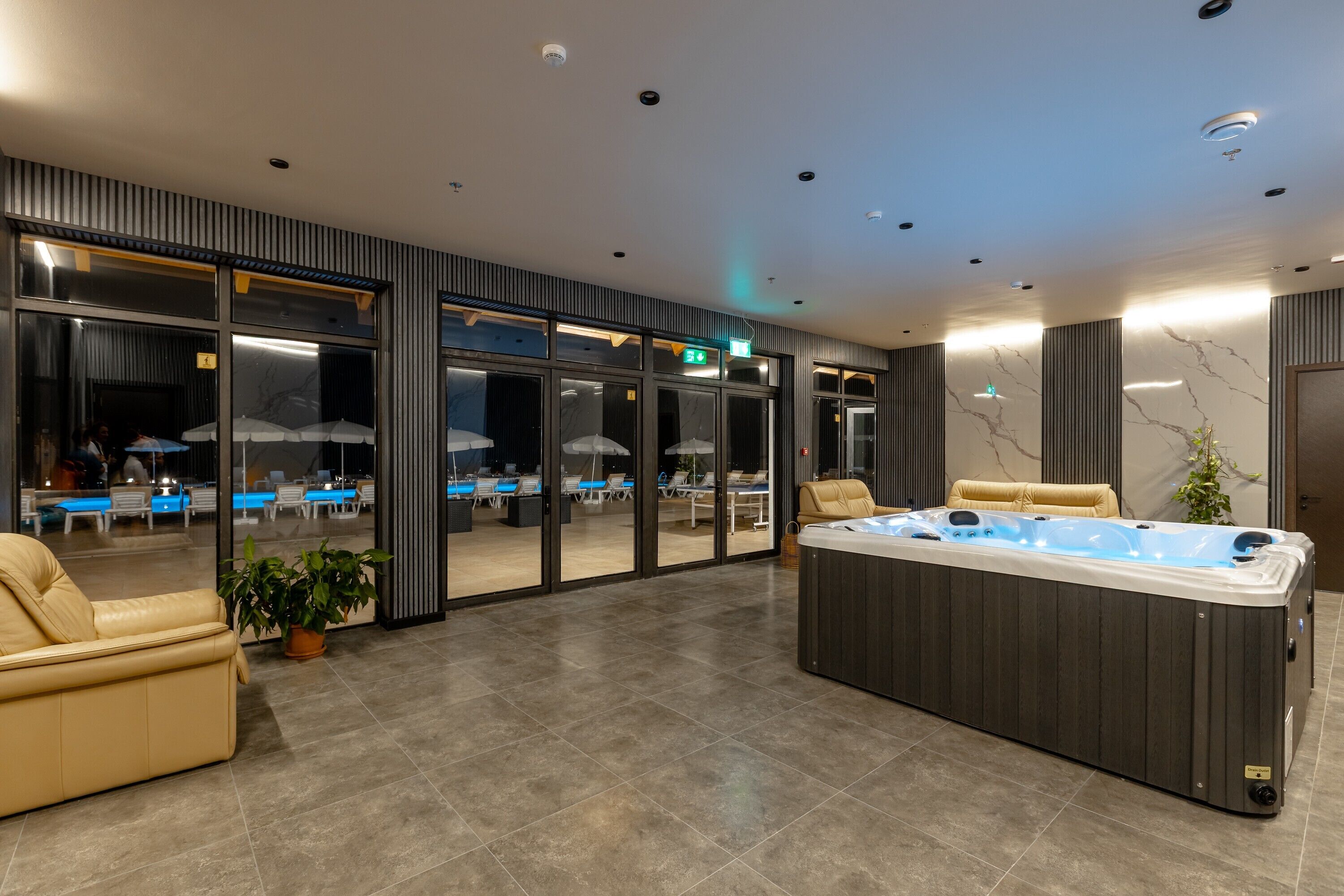 Ein moderner Poolbereich im Innenbereich mit Whirlpool, Sitzgelegenheiten und einem durch eine Glaswand abgetrennten Essbereich.